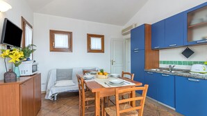 Une cuisine compacte avec des meubles bleus, une table à manger pour quatre personnes, un four à micro-ondes et un téléviseur posé sur un meuble en bois.