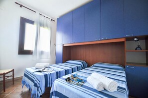 Hotelkamer met twee bedden, een houten hoofdeinde, een raam met gordijnen en een bureau met stoel.