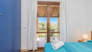 Een slaapkamer met een bed, een blauwe garderobe, een raam met gordijnen en uitzicht op de omgeving.