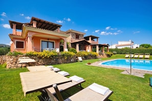 A villa with a swimming pool, outdoor seating, and a stone wall.