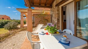 A patio with a table set for two, a potted plant, and a glass of orange juice. - Le Dimore di Nettuno 2 With Pool, Pittulongu, Italy (Pittulongu)