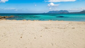 A beach with clear turquoise water, sandy shore, and distant mountains. - Le Dimore di Nettuno 2 With Pool, Pittulongu, Italy (Pittulongu)