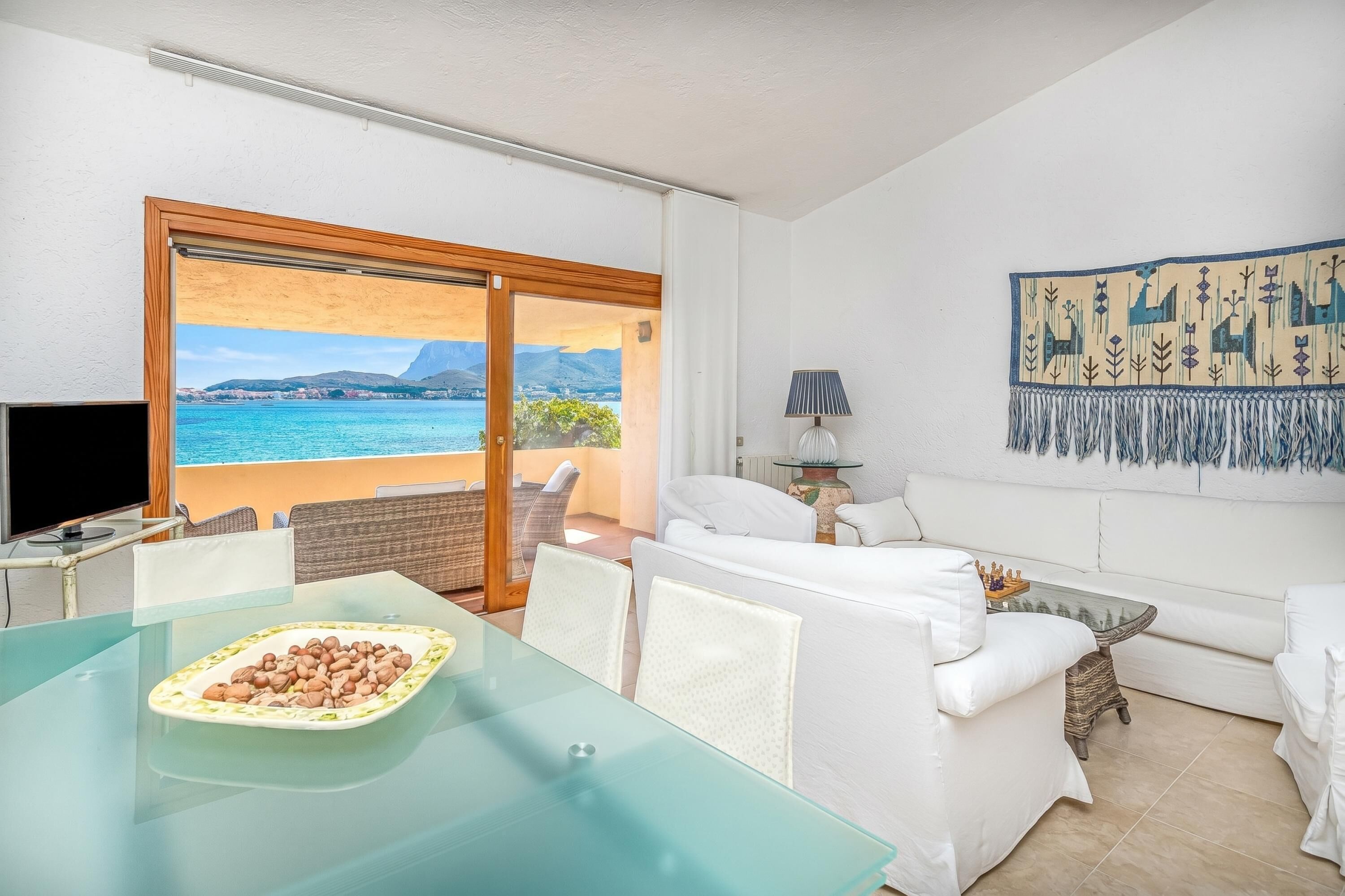 Une pièce avec une table en verre, un canapé blanc et une vue sur la mer.