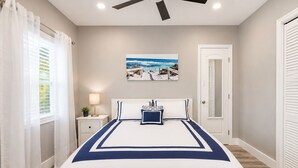 A bedroom with a bed, a nightstand, a ceiling fan, a window with curtains, and a door. - Poinsettia Paradise - 2 BDR Wing Near Beach (Fort Lauderdale)