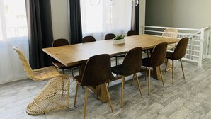 Ein Essbereich mit einem Holztisch, braunen Stühlen, einem Korbstuhl und einem weißen Geländer.