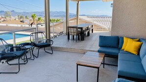 Ein überdachter Patio-Bereich mit Pool, Gartenmöbeln und Blick auf Berge.