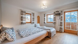 Een slaapkamer met een houten bed, twee raamdecoratie voorzien van gordijnen, een houten plafond en uitzicht op bergen.