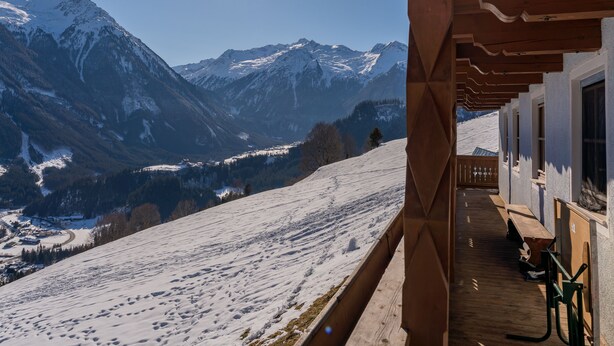 Een houten chalet met een balkon met uitzicht op een besneeuwd berglandschap.