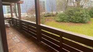 A covered outdoor area with a wooden railing, a tiled floor, and a view of a grassy area with trees and a building in the background. - Vacation apartment Leo, 65 sqm 1st floor, 2 bedrooms (Bad Endorf)