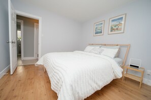 A bedroom with a wooden bed, white bedding, a bedside table with a lamp, and two framed pictures on the wall. - Cozy 3 Bedroom Contemporary Home With Free Parking  (Edmonton)