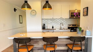 A modern kitchen with a central island, bar stools, pendant lighting, and a microwave.