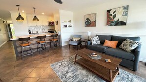 A modern living room with a dark grey sofa, a wooden coffee table, and a kitchen area in the background.