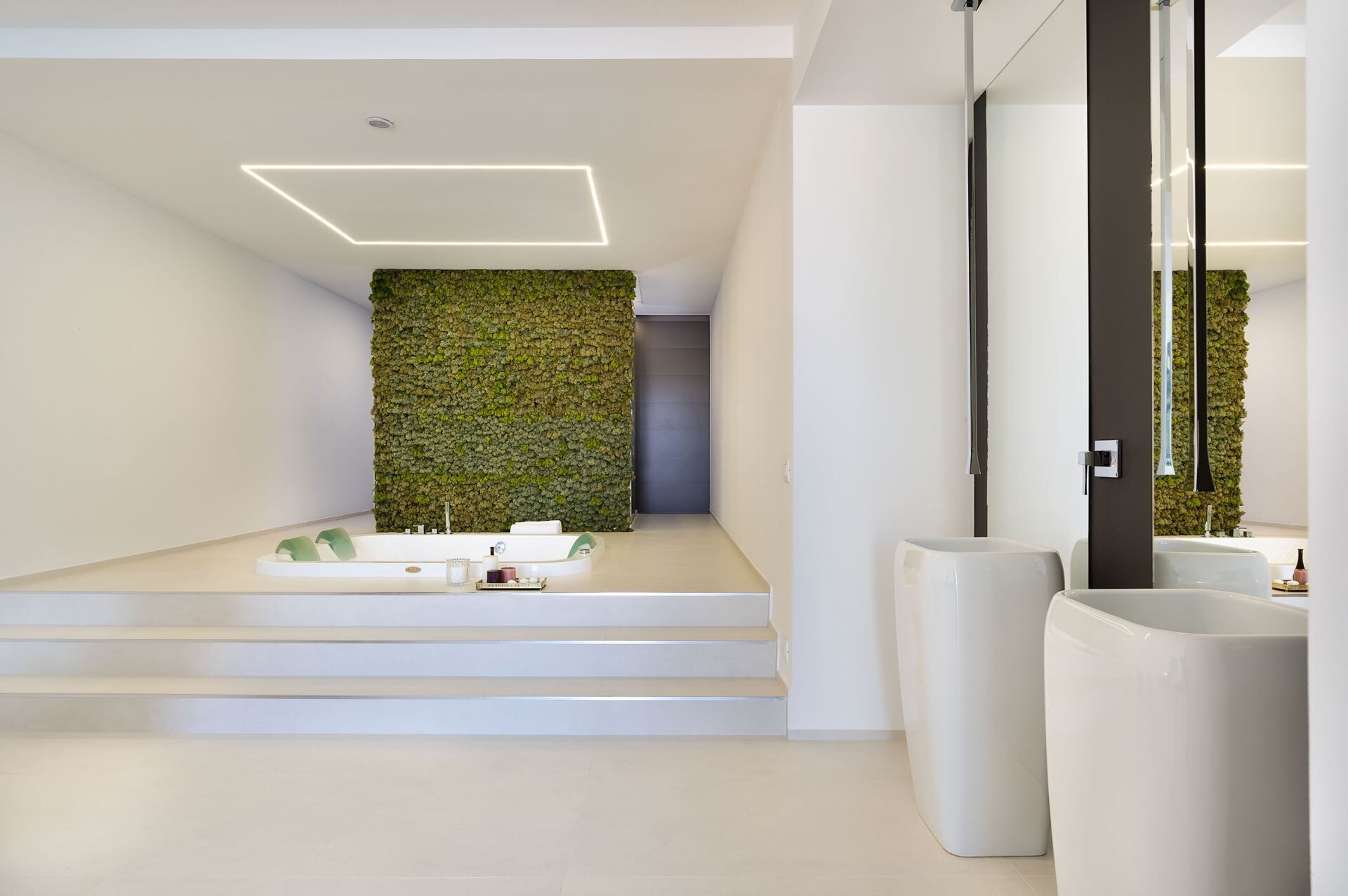 Une salle de bain moderne avec un mur recouvert de mousse verte, un lavabo blanc et un grand miroir.