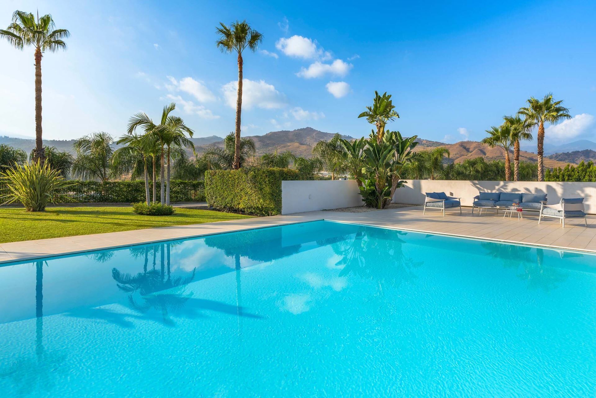 A clear blue swimming pool with lounge chairs and palm trees.