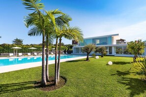 Une maison moderne avec une piscine, entourée d’une pelouse bien entretenue et de palmiers.