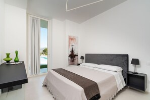 Une chambre moderne avec un grand lit, une table de chevet agrémentée de vases décoratifs, un tableau et une vue sur une piscine, visible à travers une porte coulissante.