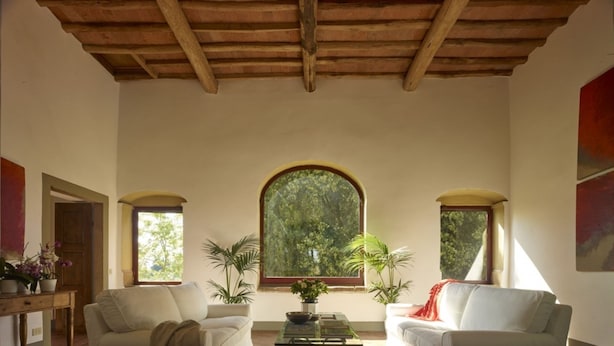 Amplia sala de estar con techo de madera alto, dos sofás blancos, una mesa de centro y un amplio ventanal de arco con vistas a la vegetación.