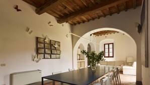 Un comedor con una mesa larga, sillas blancas, un florero con flores y un techo rústico.
