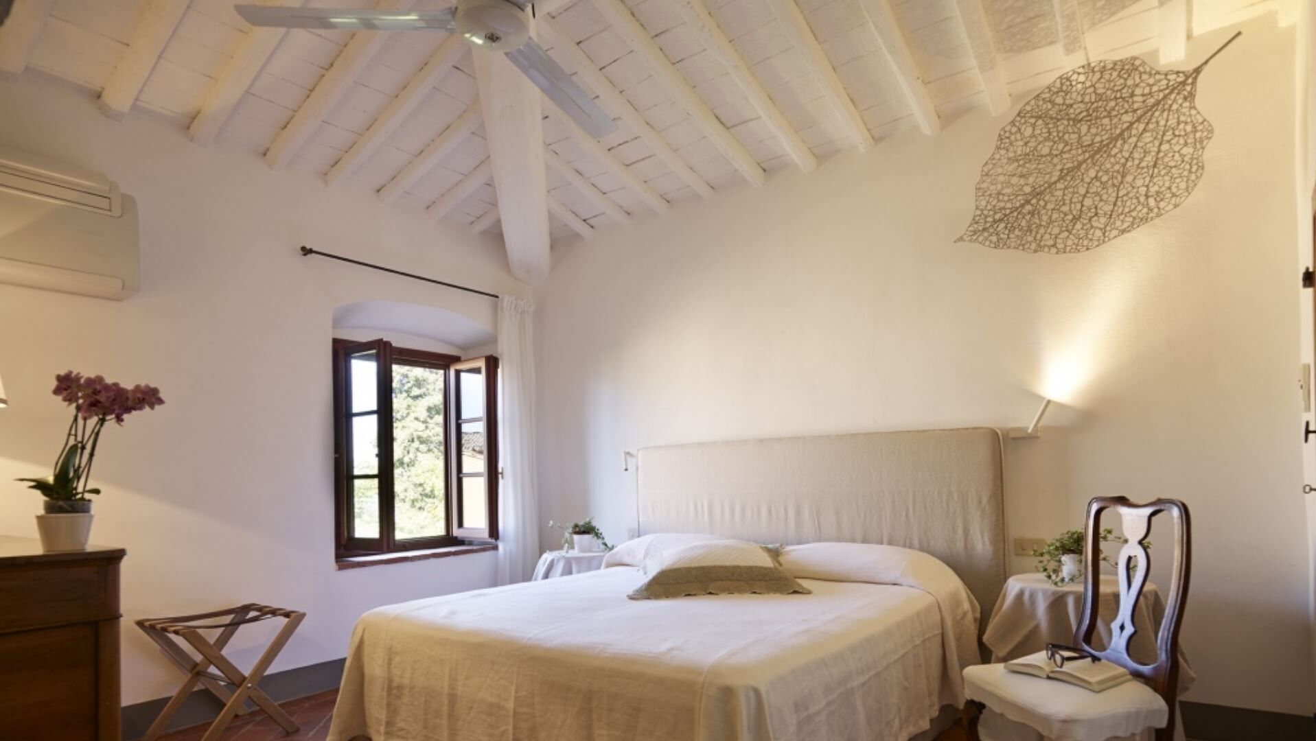 A bedroom with a large bed, a ceiling fan, a window with curtains, and a potted plant.