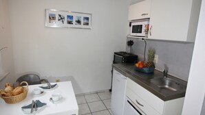 Cuina petita amb armaris blancs, microones, rentapesos i zona de dinar amb taula per a dues persones.