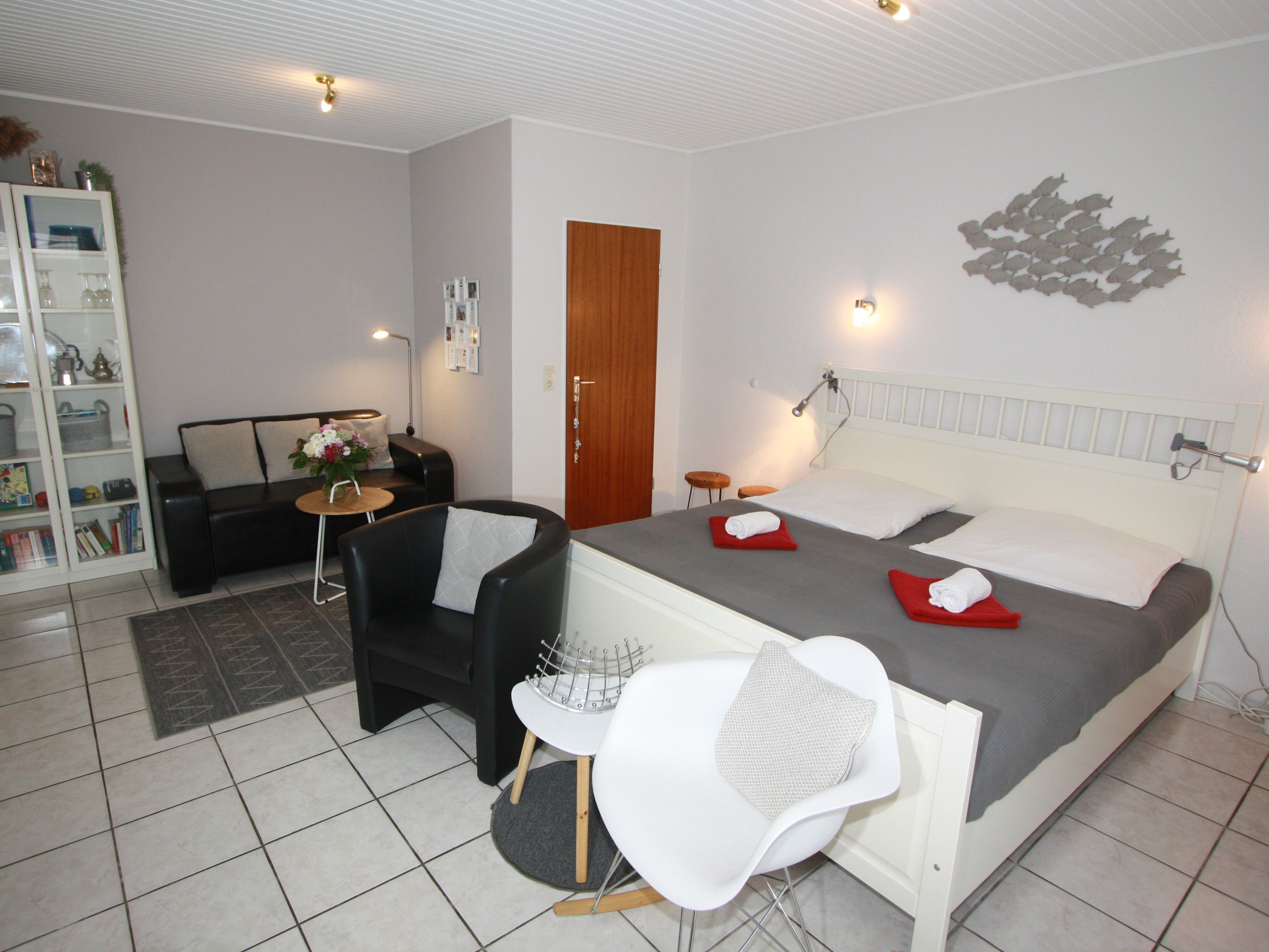 A modern hotel room with a bed, a sofa, a chair, a small table, and a bookshelf.