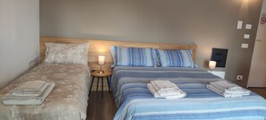 A double room with two beds, each with a pillow and a folded towel. There is a nightstand with a lamp between the beds.