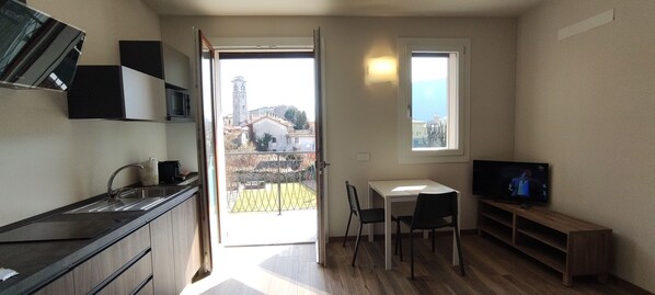A compact kitchen with a sink, cabinets, and a TV. There's a balcony with a view of buildings and a tower.