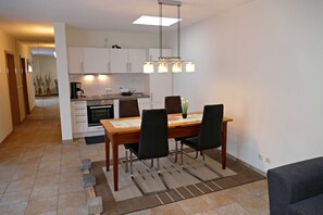 Een moderne keuken met witte kasten, een eettafel met stoelen en een hanglamp.
