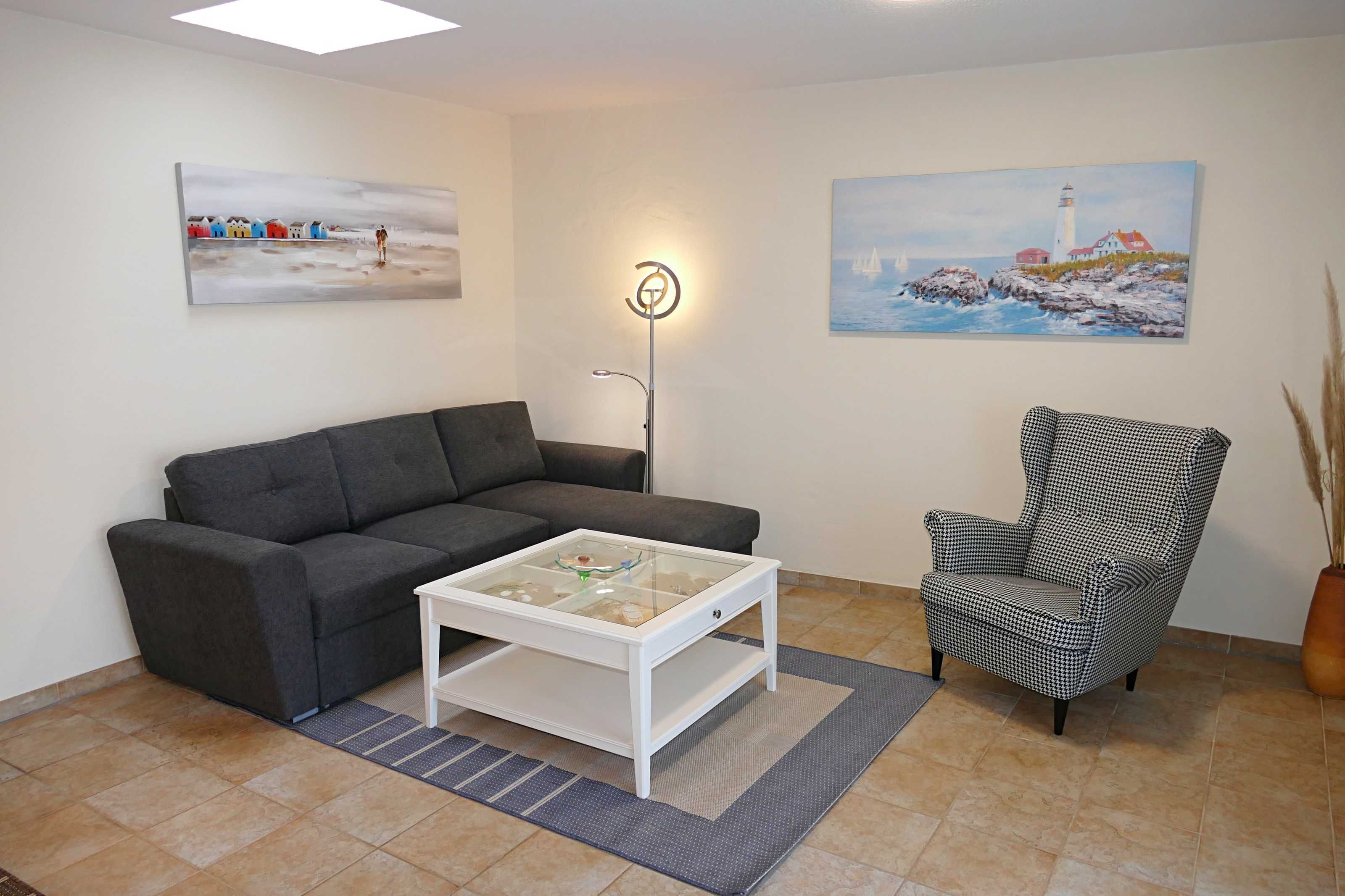 Ein Wohnzimmer mit grauem Sofa, einem weißen Couchtisch, einem karierten Sessel und zwei Bildern an den Wänden.