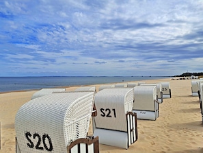 Beachside wicker chairs with price tags, arranged on a sandy beach with a view of the sea.