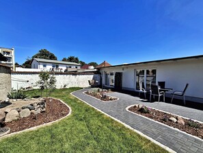 Ein Garten mit gepflasterter Terrasse, kleinem Garten und einem weißen Gebäude mit Fenster und Tür.