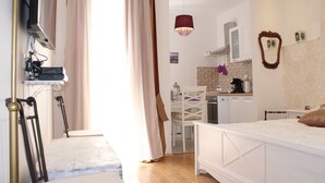 A bedroom with a bed, a bedside table, a chair, a desk, and a kitchen area with cabinets and a hanging light fixture. - Studio apartment Miko - top location, great place to enjoy (Split)