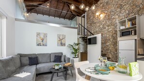 A modern living space with a grey sectional sofa, a round dining table with chairs, a small side table, a potted plant, and artwork on the walls. - EPTA Houses (KOS)