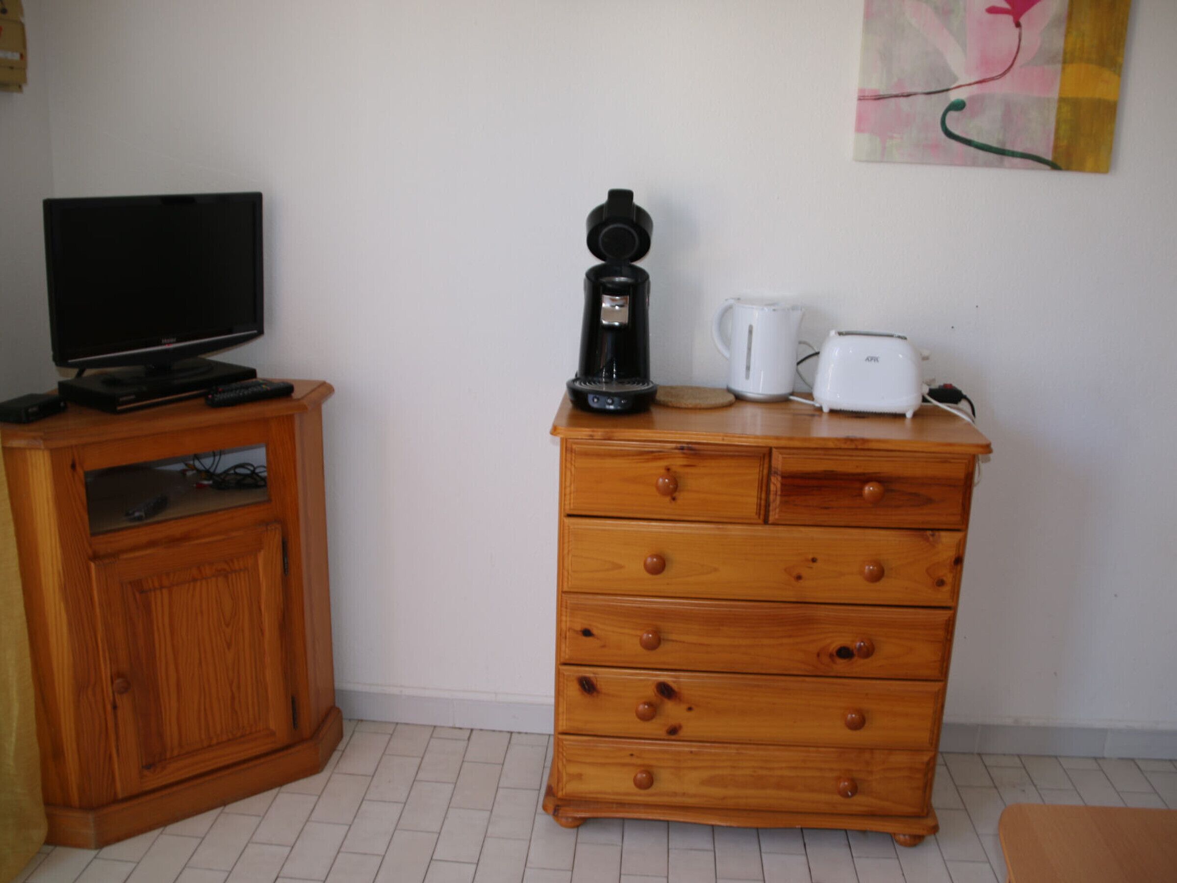 A wooden dresser with drawers, a television on a cabinet, a coffee maker, and a toaster on the dresser.