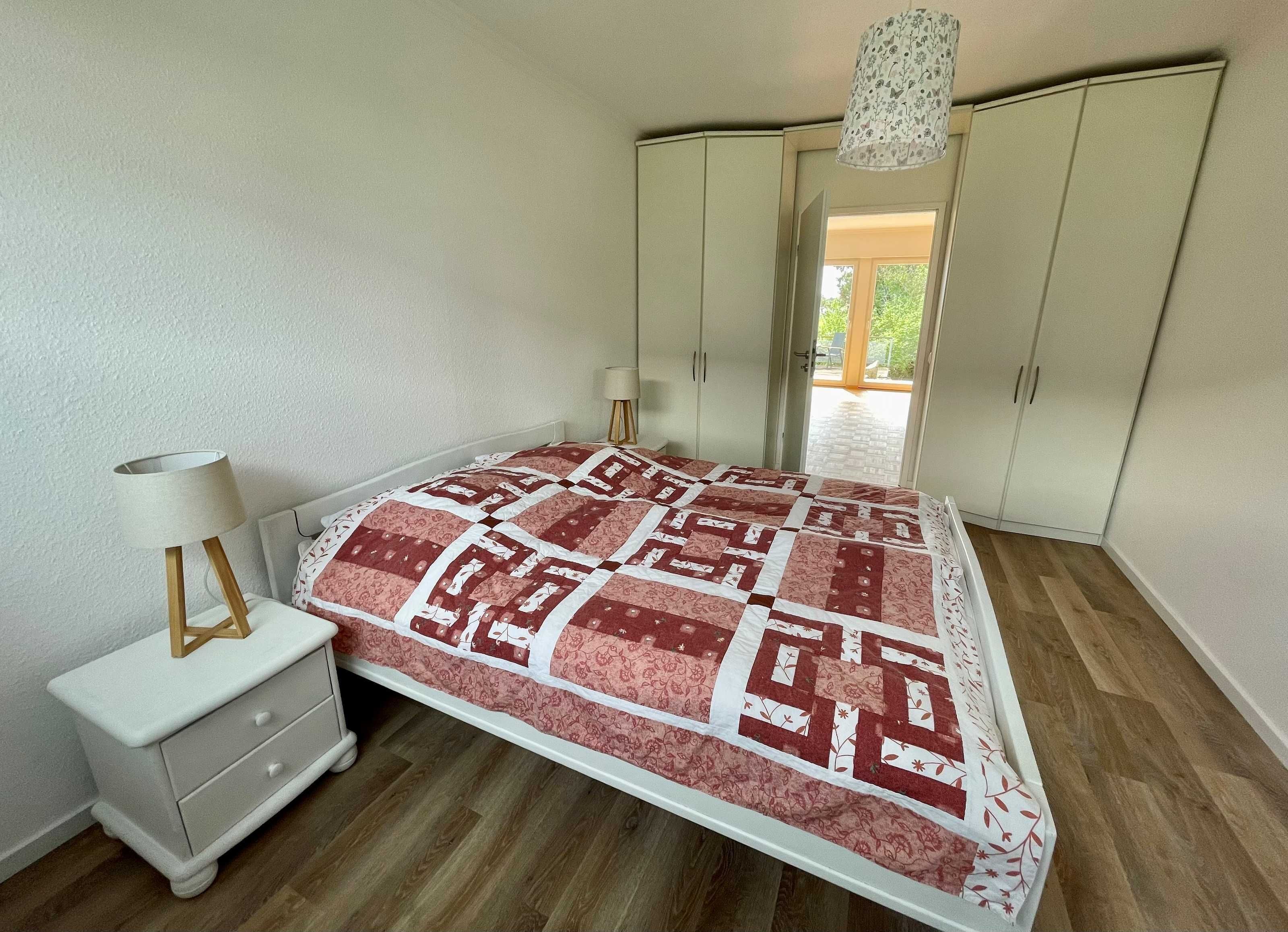Een slaapkamer met een bed, nachtkastje, lamp, kledingkast en uitzicht op de omgeving.