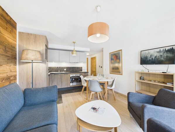 A modern living room with a dining area, kitchen, and a TV mounted on the wall.