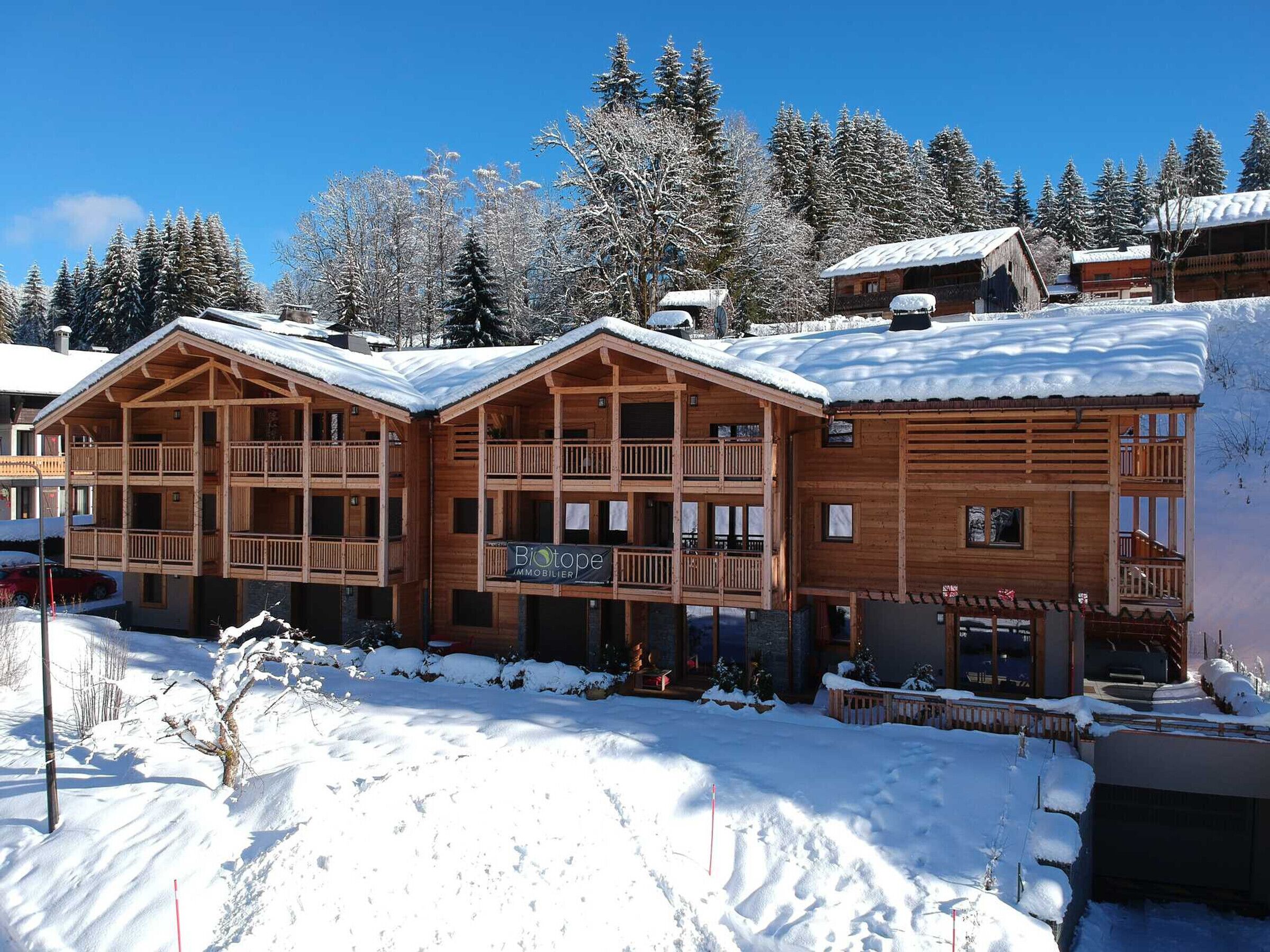 A wooden chalet with multiple balconies and a snow-covered roof, surrounded by trees.