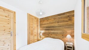 Une chambre avec un mur recouvert de lambris en bois, un lit avec une couvre-lit blanche, une table de chevet avec une lampe et une porte en bois.