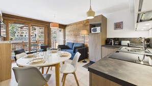 Une cuisine moderne équipée d’un four à micro-ondes encastré, un coin repas avec une table ronde et des chaises, et un salon avec un canapé et une lampe.