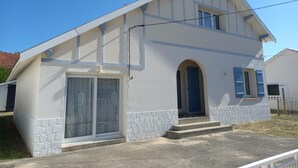 A two-story house with a stone foundation, a front door with a blue shutter, and a large window with a curtain.
