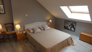 A bedroom with a sloped ceiling, a skylight, a bed with a patterned headboard, two bedside tables with lamps, and a framed picture on the wall.