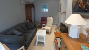 A living room with a grey sofa, a white table, a red chair, a wooden cabinet, and a painting on the wall.