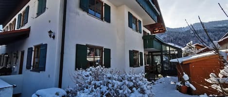 A two-story building with multiple windows, a balcony, and a snow-covered garden.
