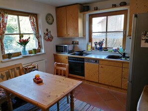 A kitchen with wooden cabinets, a microwave, a sink, and a dining table with fruit. - Constance mountain view with winter garden (Oberstaufen)