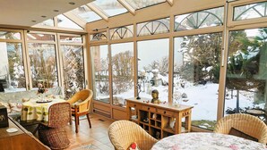 A sunroom with large windows, wicker furniture, and a view of a snowy garden. - Constance mountain view with winter garden (Oberstaufen)