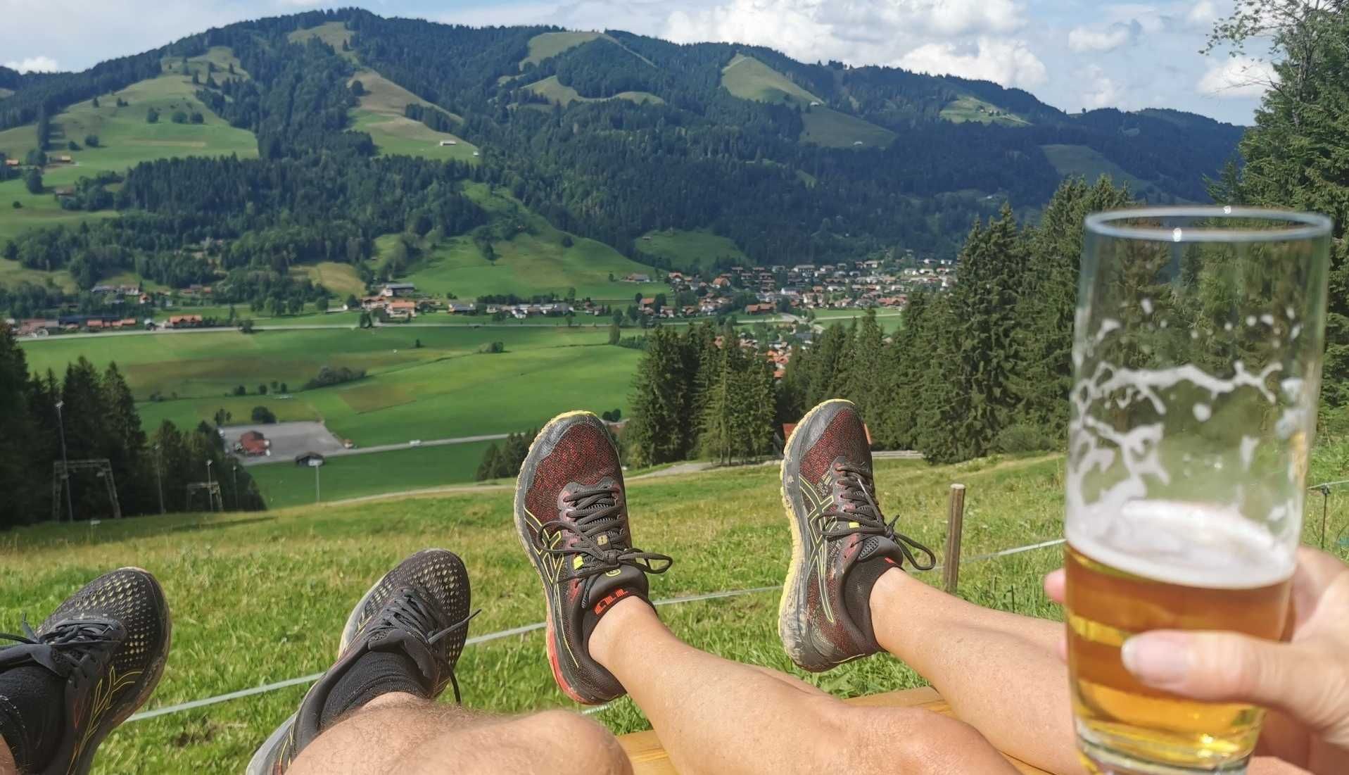 A person relaxing with legs propped up, overlooking a scenic mountainous landscape with a village below.