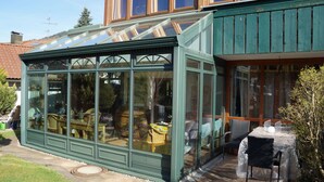 A conservatory with a glass roof, wooden furniture, and a small table. - Constance mountain view with winter garden (Oberstaufen)