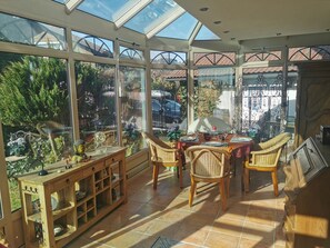 A sunlit room with large windows, wicker furniture, and a wooden table set for dining. - Constance mountain view with winter garden (Oberstaufen)