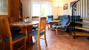 Een gezellige woonkamer met een houten eettafel, blauwe fauteuils, een blauwe bank en een trap.