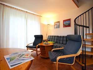 Una sala de estar con una mesa de madera, dos sillones, un sofá, una lámpara y una escalera.